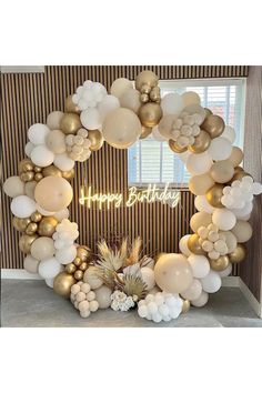 a white and gold balloon arch with the words happy birthday written in front of it