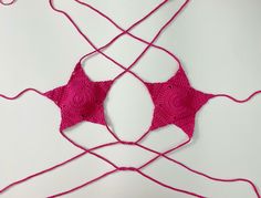 there is a pink crocheted bralet on the white surface with red thread