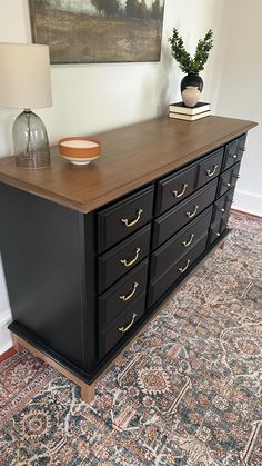 a black dresser with gold handles and drawers in a room next to a painting on the wall