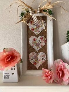 some flowers are sitting on a shelf next to a picture frame with hearts and ribbons