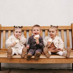 three children sitting on a bench eating ice cream