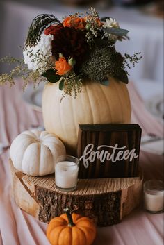 a table topped with a wooden sign and pumpkins next to candles on top of a piece of wood