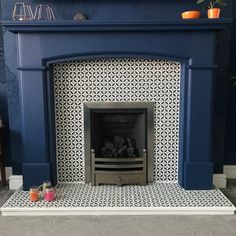 a blue fireplace with white and black tiles on the mantle, next to a potted plant