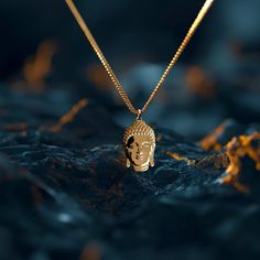 a golden buddha head pendant on a gold plated chain with water in the background