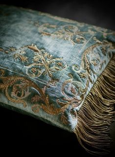 a blue and gold pillow with fringes on it's sides, sitting on a black surface