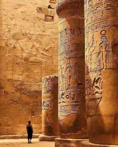 an ancient egyptian temple with columns and carvings on the walls, in front of a man standing next to it