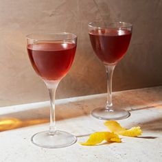 two wine glasses filled with red wine and orange peels next to each other on a counter