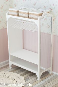 a small white shelf with clothes hanging on it's sides in front of a floral wallpapered wall