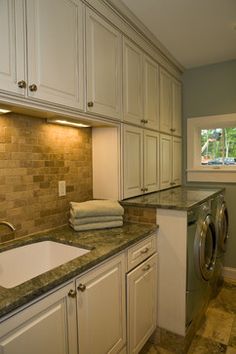 a washer and dryer in a kitchen with white cabinets, granite counter tops