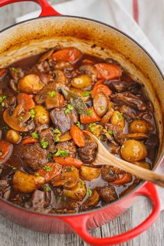 beef stew with carrots, potatoes and parsley in a red pot on a wooden table