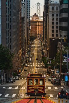 a trolley car traveling down a city street next to tall buildings and traffic lights in the distance