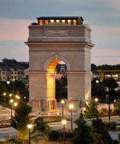 a clock tower lit up at night with lights on it's sides and an american flag in the foreground