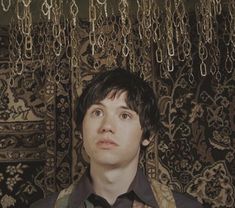 a young man standing in front of a wall covered with gold chandelier hanging from it's ceiling