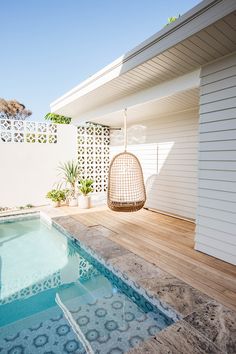 a pool with a hanging chair next to it and a white house in the background