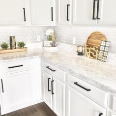 a white kitchen with marble counter tops and black pulls on the cabinet doors is shown