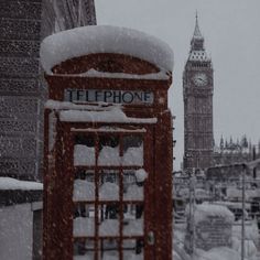 a phone booth covered in snow next to a clock tower