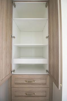 an empty closet with wooden drawers and white shelves on the door, in front of a wall