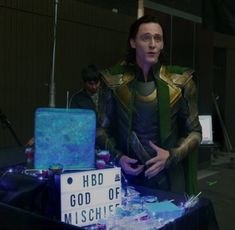 a man dressed as loki in front of a table with a sign that says hod the god of misshkens