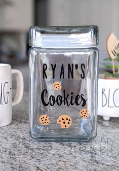 a glass jar with cookies on it next to two mugs