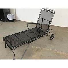 a wrought iron chaise lounge chair sitting on the concrete floor next to a trash can