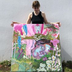 a woman is holding up a painting with flowers and plants on it, in front of a white wall