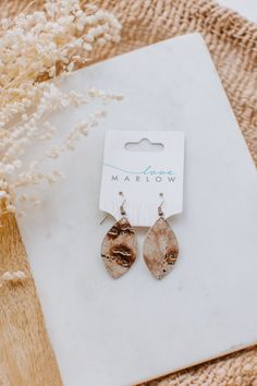 two pairs of earrings sitting on top of a piece of paper next to some dried flowers