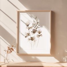 a framed art print on a wall above a shelf with a vase and plant in it