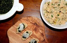 some food is sitting on a wooden board next to a bowl of soup and a plate of spinach