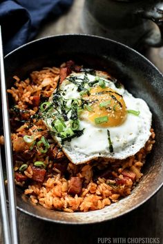 fried eggs and rice in a skillet with chopsticks