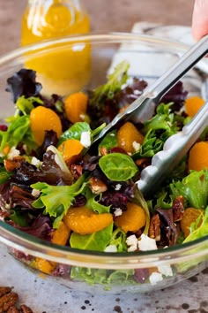 a salad with oranges, lettuce and feta cheese in a glass bowl