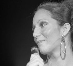 a woman holding a microphone in her right hand and wearing earrings on top of her head