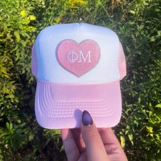 a person holding up a pink and white trucker hat with the letter dm on it