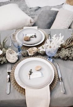 the table is set with plates, silverware and sea shells on it's placemats