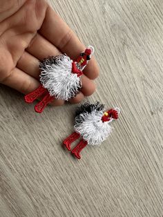 two small red and white roosters are held in someone's hand on a wooden surface