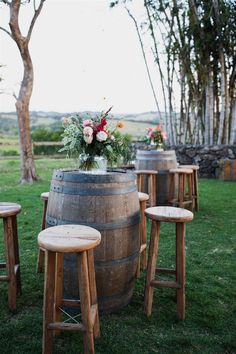 wooden stools sit in front of an old barrel with flowers on it and greenery