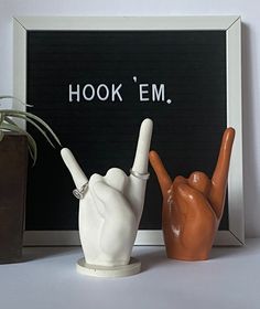 two ceramic hand gestures in front of a sign that says hook'em