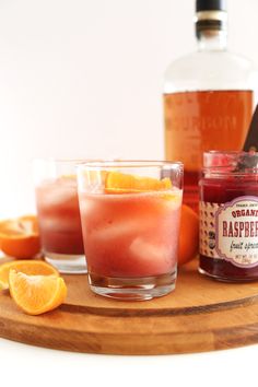 two glasses filled with liquid sitting on top of a wooden tray next to orange slices