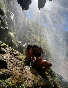 two women are sitting on the rocks in front of water spewing from them