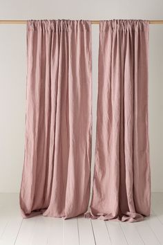 two pink curtains hanging on a wooden rail in front of a white wall and floor