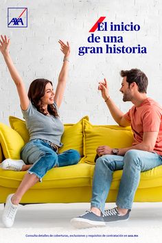 a man and woman sitting on a yellow couch with their arms up in the air