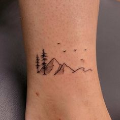 a tattoo on the foot of a person with mountains and birds in the sky behind them