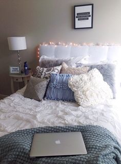 a laptop computer sitting on top of a bed covered in pillows and blankets with lights