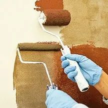 a person in blue gloves painting a wall with brown and white paint on the walls