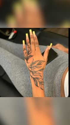 a woman's hand with yellow fingernails and tattoos