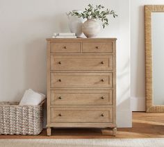 a white vase sitting on top of a wooden dresser next to a basket and mirror