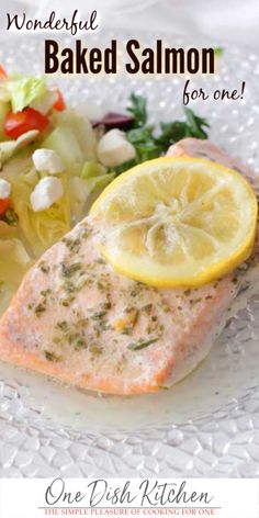 a white plate topped with salmon and salad next to a lemon wedge on top of lettuce