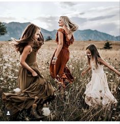 three beautiful women in long dresses walking through a field