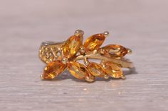 This stunning piece, known as The Golden Leaf, features an arrangement of marquise-cut citrines designed to resemble a delicate leaf motif. The vibrant citrines, with their warm golden hues, are elegantly set in a 14 karat yellow gold band, creating a piece that exudes natural beauty and elegance. This exquisite ring is currently a finger size 4.75 yet can be adjusted to any finger size for an additional charge upon request, ensuring a perfect fit. Love this piece, but don't have the money to spend right now? We offer FREE layaway on every item in our shop. With just 20% down, take one full year (interest-free) to pay off your new jewelry! There are no hidden fees or charges, ever. For more information on our layaway policy, please contact us. Each piece has been hand-selected and meticulo Citrine Marquise Ring, Leaf Wedding Rings, Golden Leaf, Marquise Ring, Leaf Motif, Citrine Ring, Marquise Cut, Gold Band, Rings Statement