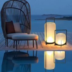 two lit candles sitting on top of a wooden deck next to a chair and table