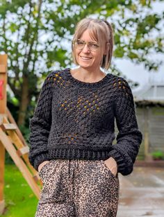 a woman standing in front of a wooden structure wearing leopard print pants and a black sweater